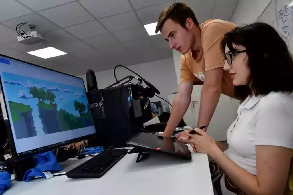 Entraide étudiante Deux étudiants en infographie travaillants ensembles sur une illustration 2D.