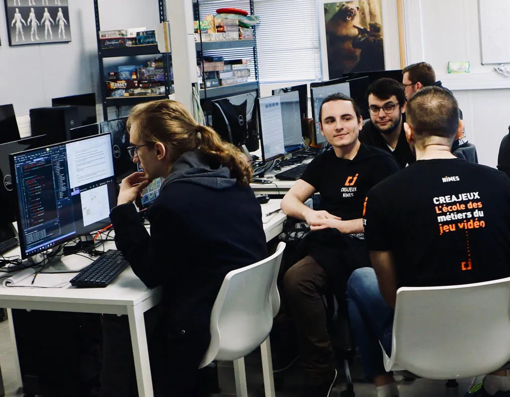 Encadrement Fred (Programmation) Salle info à Creajeux : Fred, formateur en programmation, conseille un groupe d’étudiants devant leurs postes (écrans avec code/IDE ouverts).